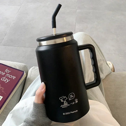 Snoopy  Black insulated mug with handle held by a person on a couch, featuring Snoopy and Woodstock design.