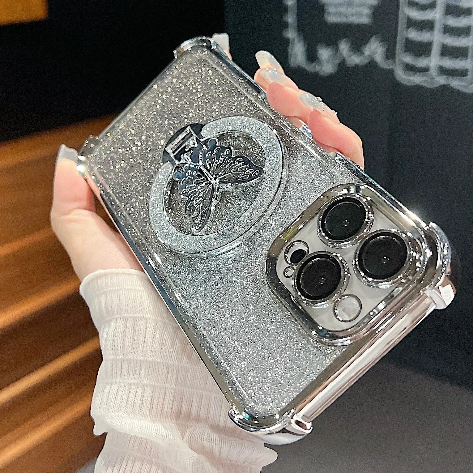 Silver glittery phone case with butterfly design held by a hand