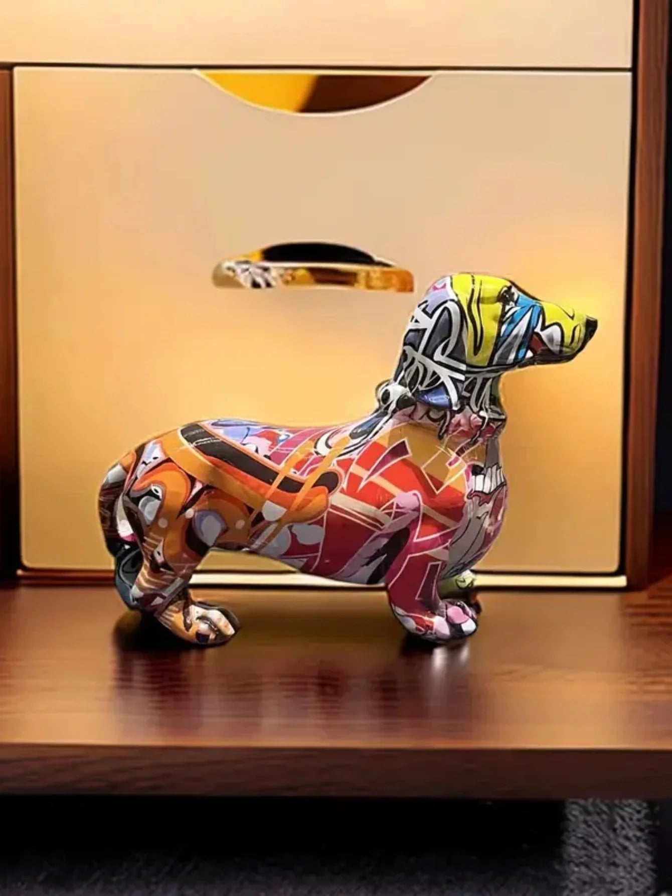 Colorful ceramic dog figurine on a wooden surface with a reflective gold background dashhound