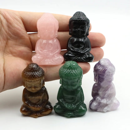 Five small stone Buddha figurines in different colors held in a hand against a white background.