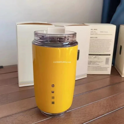 SMEG Yellow travel mug with a clear lid on a wooden surface, with a box in the background.