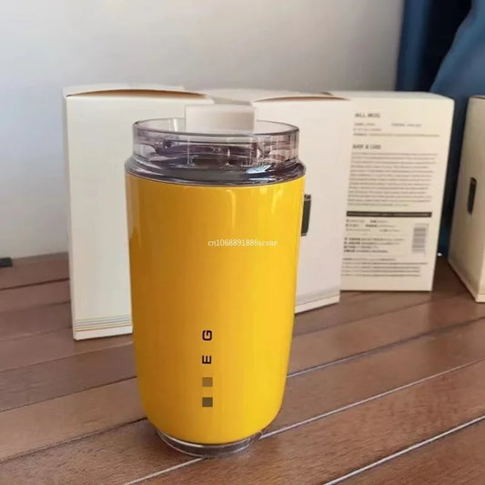 SMEG Yellow travel mug with a clear lid on a wooden surface, with a box in the background.