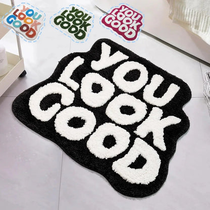 Black rug with 'YOU LOOK GOOD' text on a light gray floor, with 'YOU LOOK GOOD' motivational stickers above. bath mat