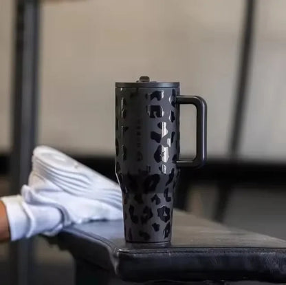 Black leopard print HydroJug Gobelet 40OZ Voyageur Thermos placed on a gym bench, showcasing its stylish and durable design.