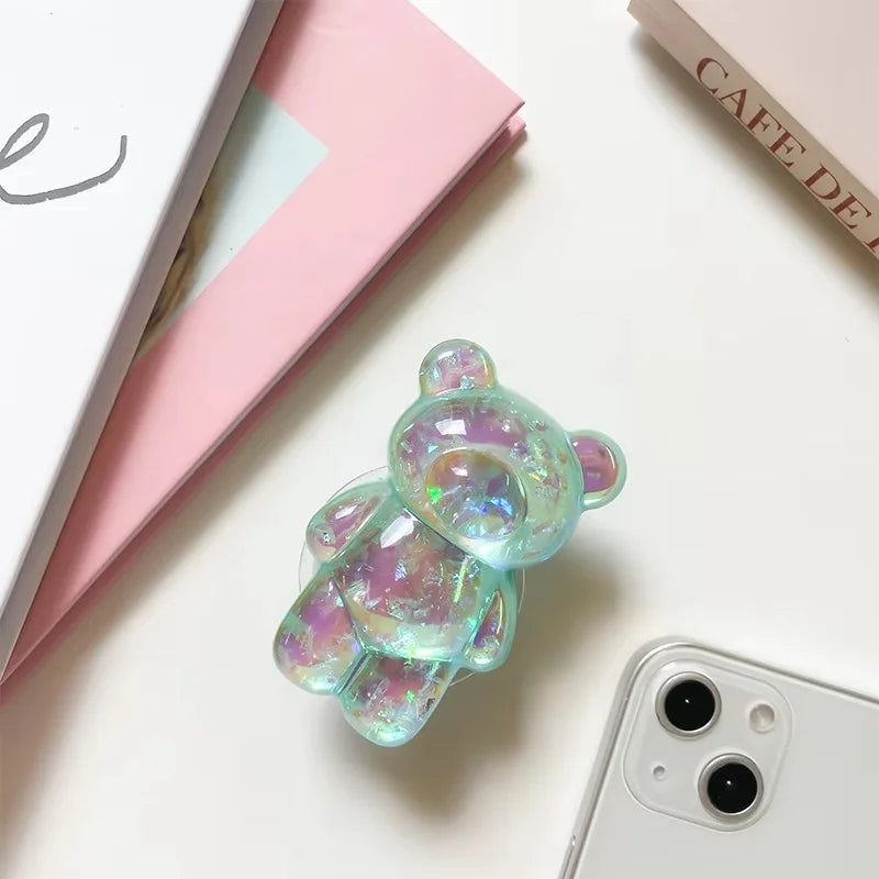 Iridescent bear-shaped phone case on a white surface with a pink book and 'Cafe Deli' menu.
