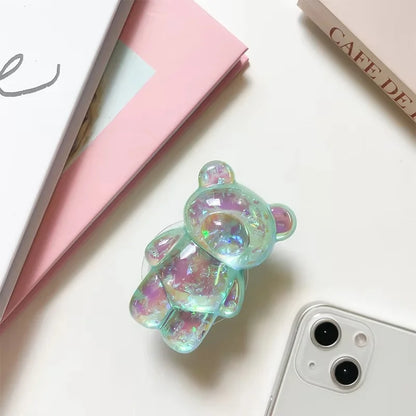 Iridescent bear-shaped phone case on a white surface with a pink book and 'Cafe Deli' menu.