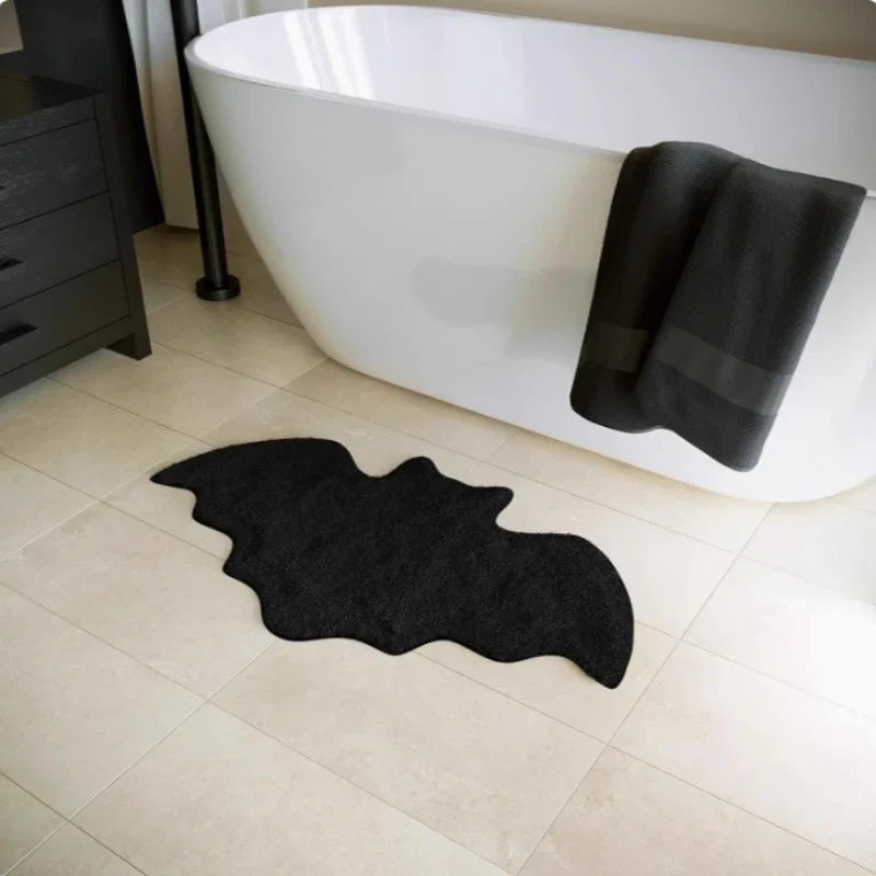 Black bat-shaped rug on a bathroom floor with a white bathtub and black towel.