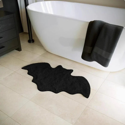 Black bat-shaped rug on a bathroom floor with a white bathtub and black towel.