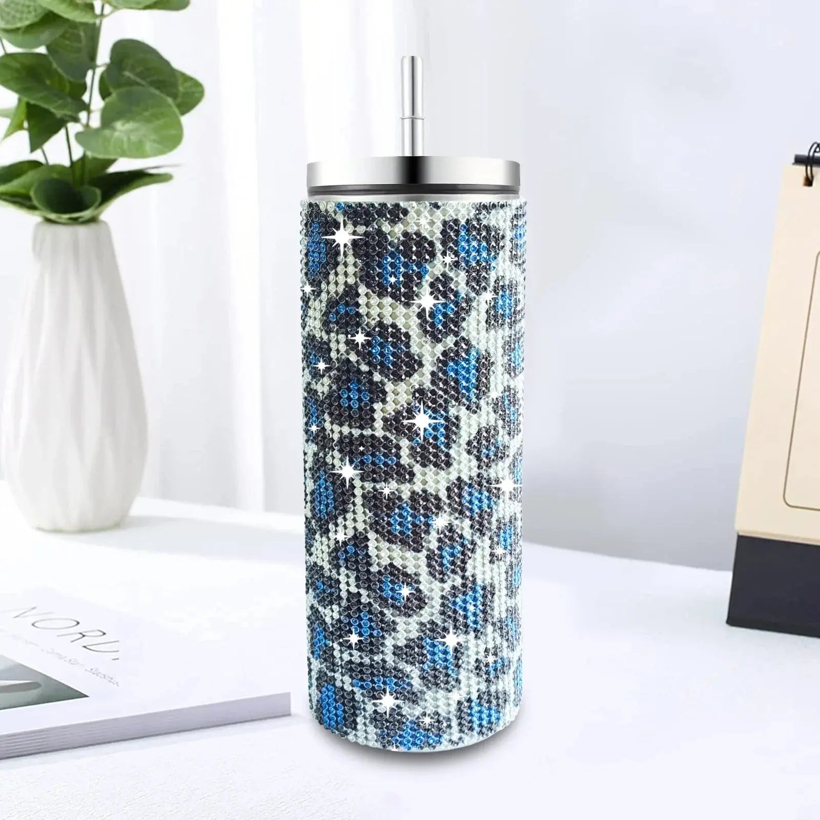 Tumbler with blue and black pattern on a white surface with a plant and notebook in the background