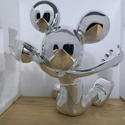 Metallic sculpture of a stylized face with circular eyes and a curved mouth on a wooden surface.