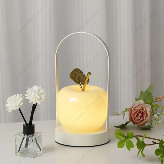 Decorative apple lamp with a leaf design on a white surface with flowers and a curtain background
