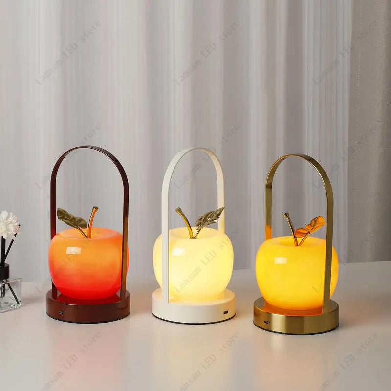 Three decorative apple-shaped lamps with different colored lights on a neutral background