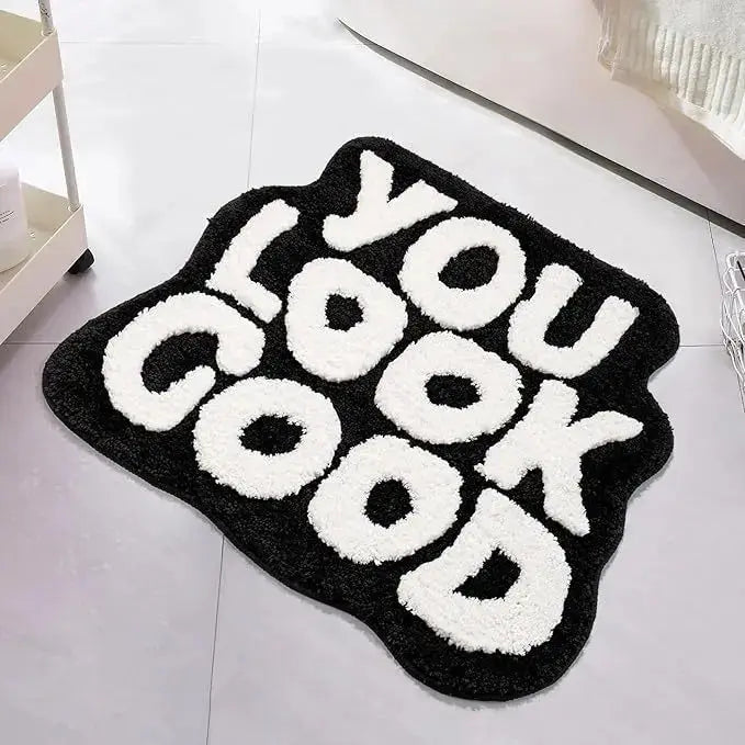 Black rug with white text 'YOU LOOK GOOD' on a light gray floor. bath mat