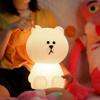 Person holding a bear-shaped night light with a plush toy in the background