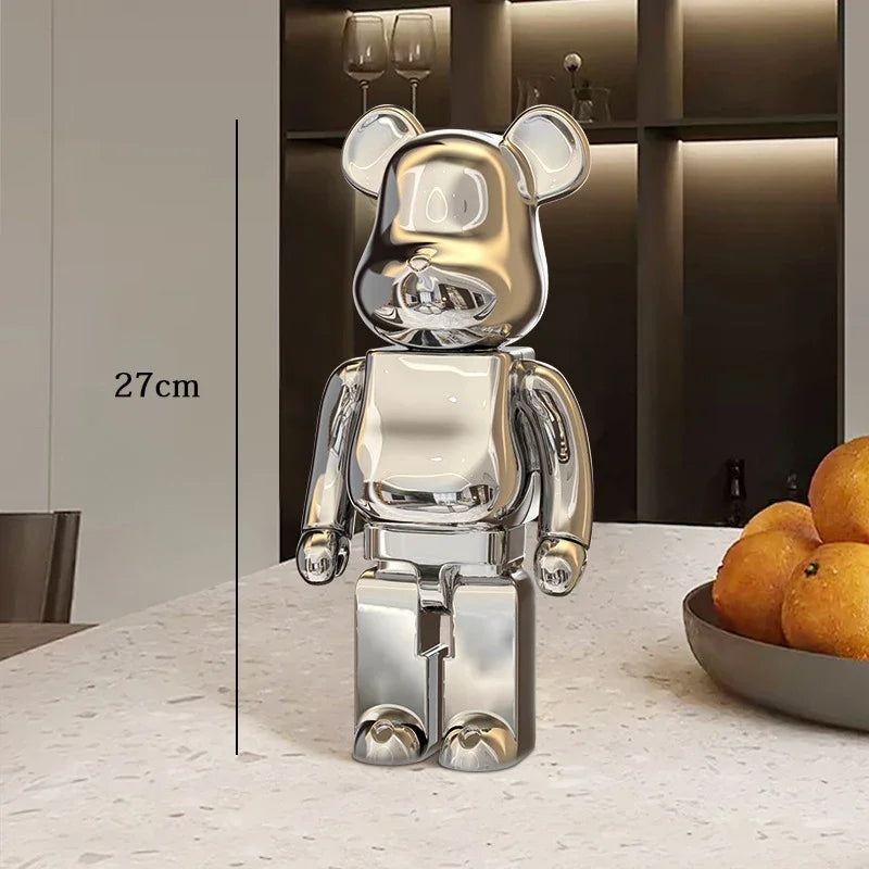 Silver bear-shaped figure on a table with a bowl of oranges in the background be@rbrick collectable