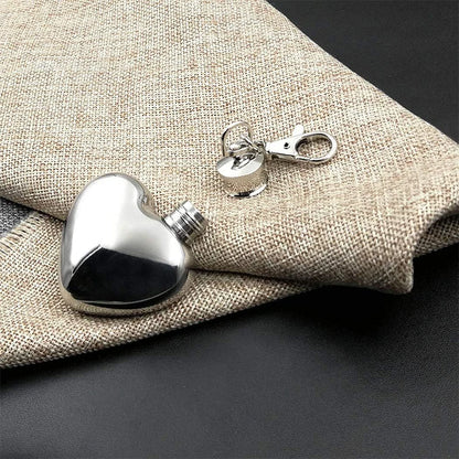 Heart-shaped silver flask with a clip on a textured fabric background