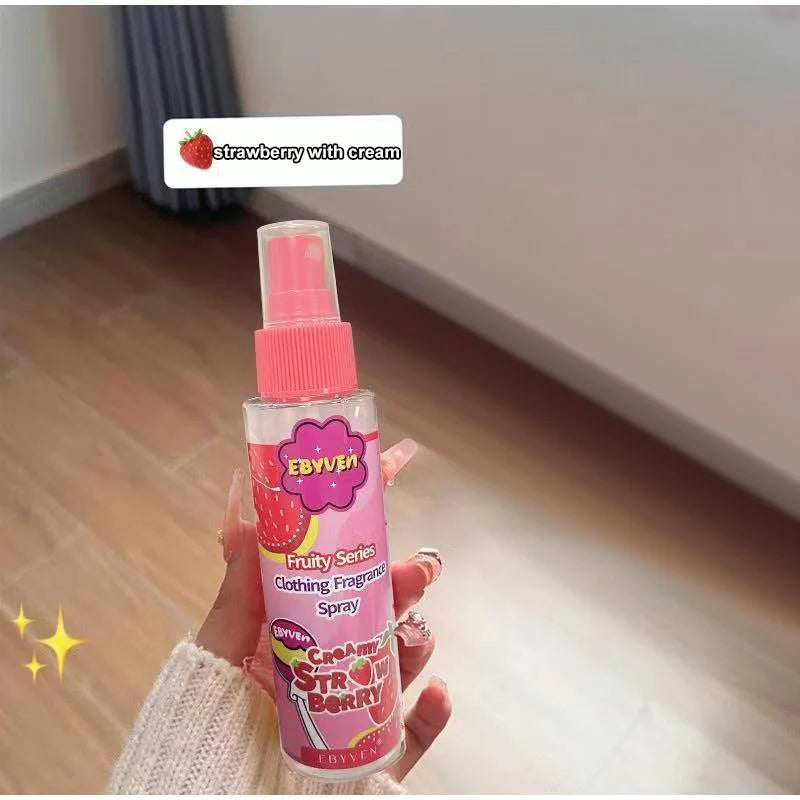 Pink clothing fragrance spray bottle labeled 'Ebyver' held by a hand on a wooden floor.