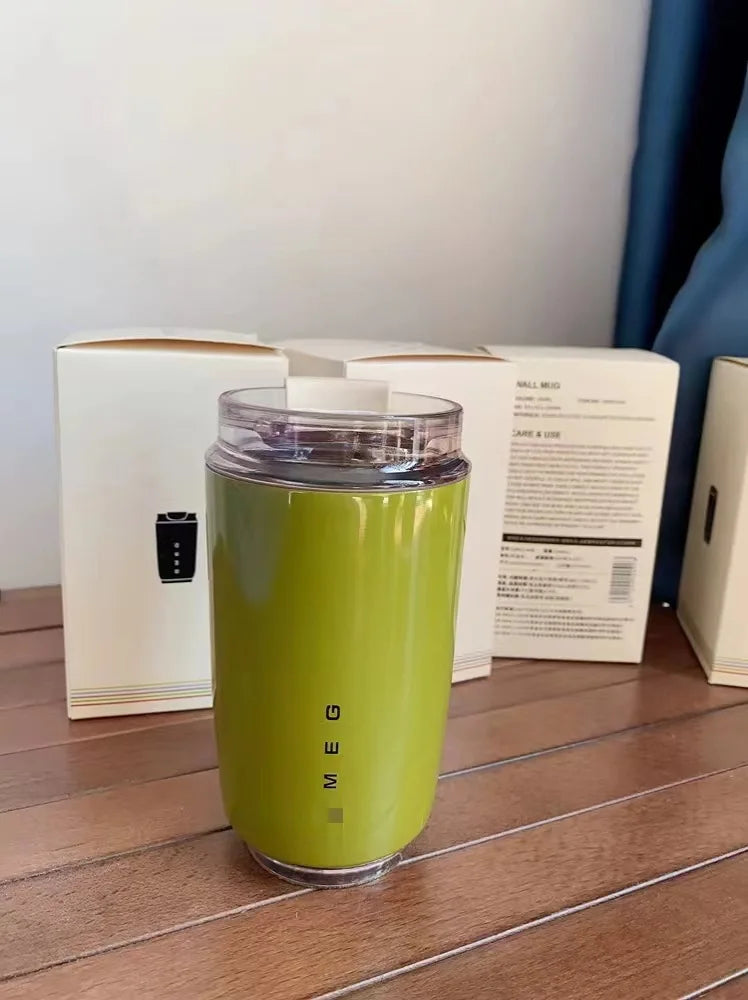 SMEG Green tumbler with clear lid on a wooden surface with boxes in the background
