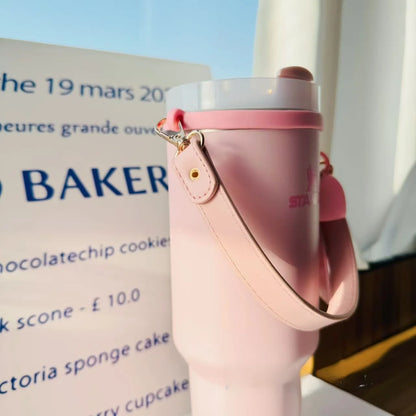 Pink water bottle with a strap held by a hand, blurred background with text and a window.