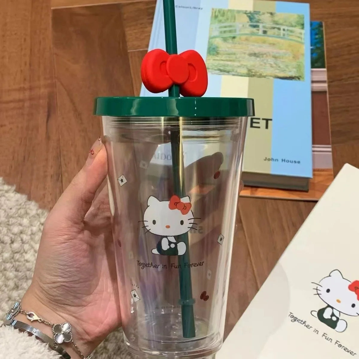 Hello Kitty Clear tumbler with Hello Kitty design held by a hand, against a wooden surface with books.