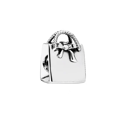 Silver charm shaped like a handbag with a bow on a white background