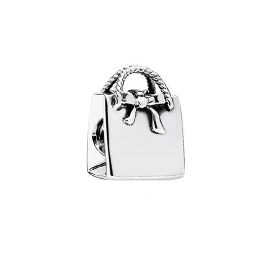 Silver charm shaped like a handbag with a bow on a white background