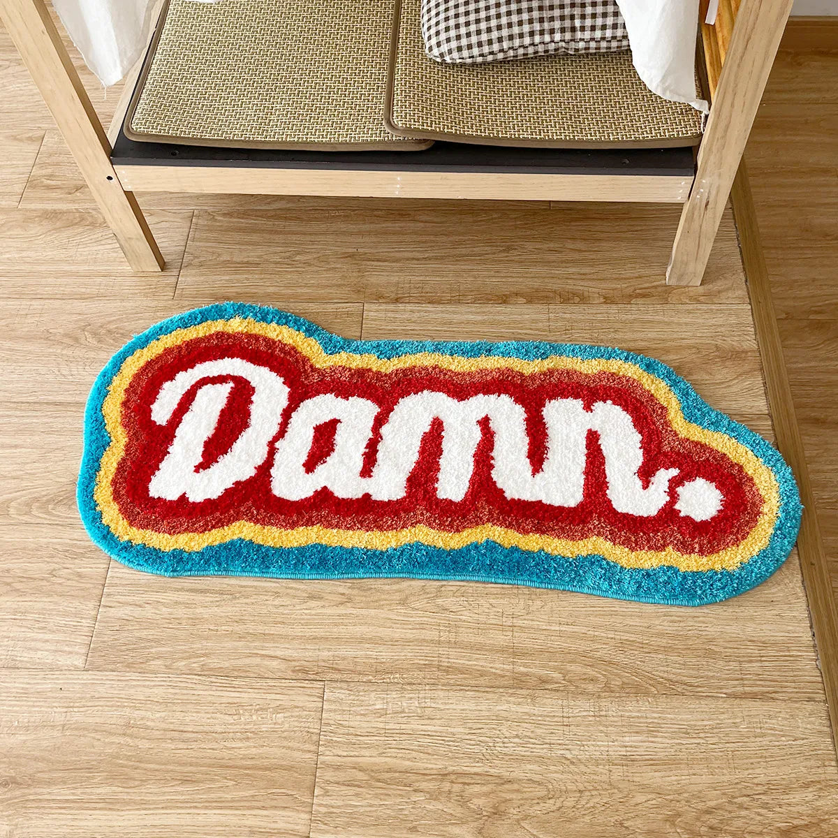 Colorful doormat with 'Damn.' text on a wooden floor