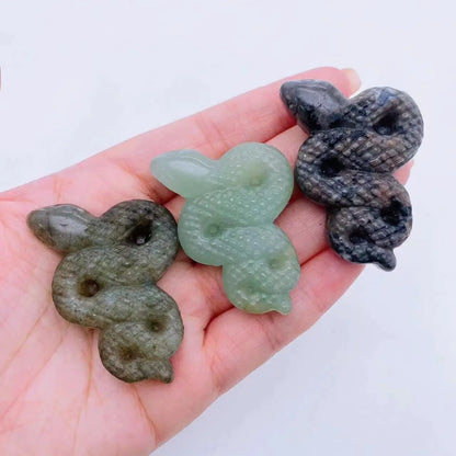 A collage of various crystal snake statues in different colors held in a person's hand.