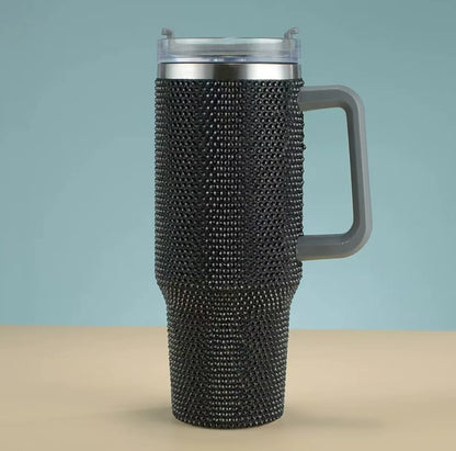 Travel mug with black rhinestone embellishments on a beige surface with a light blue background