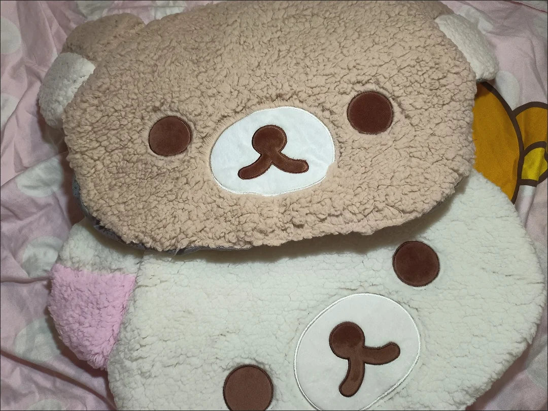 Plush toy resembling a bear with a round face and brown eyes on a pink background