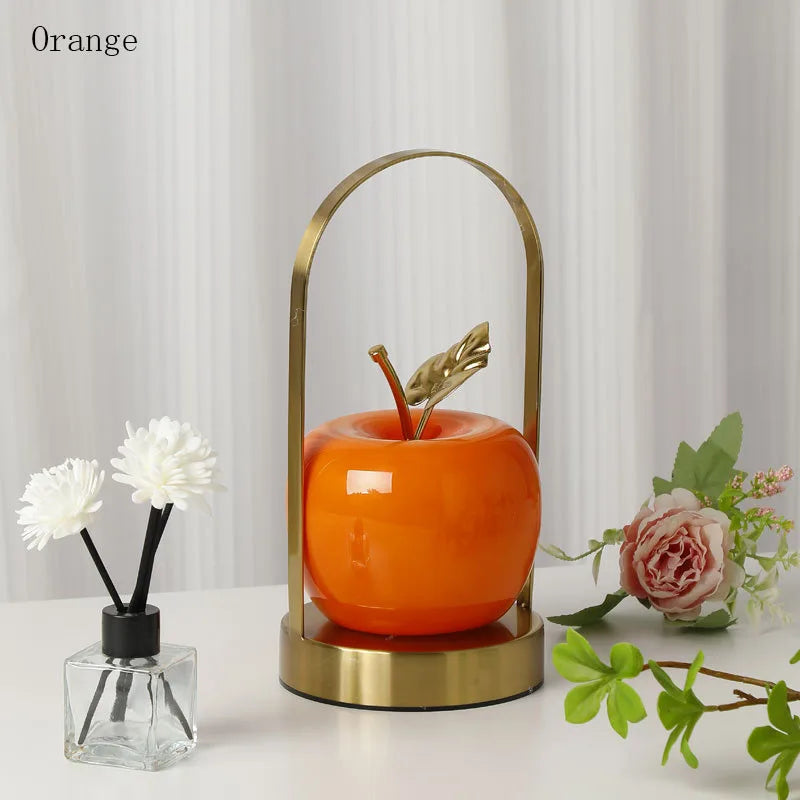Decorative apple-shaped object with gold base on a white surface with flowers.