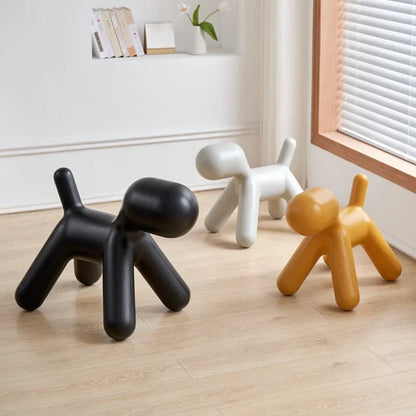 Three dog-shaped stools in black, white, and orange on a wooden floor.