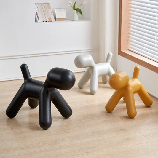 Three dog-shaped stools in black, white, and orange on a wooden floor.